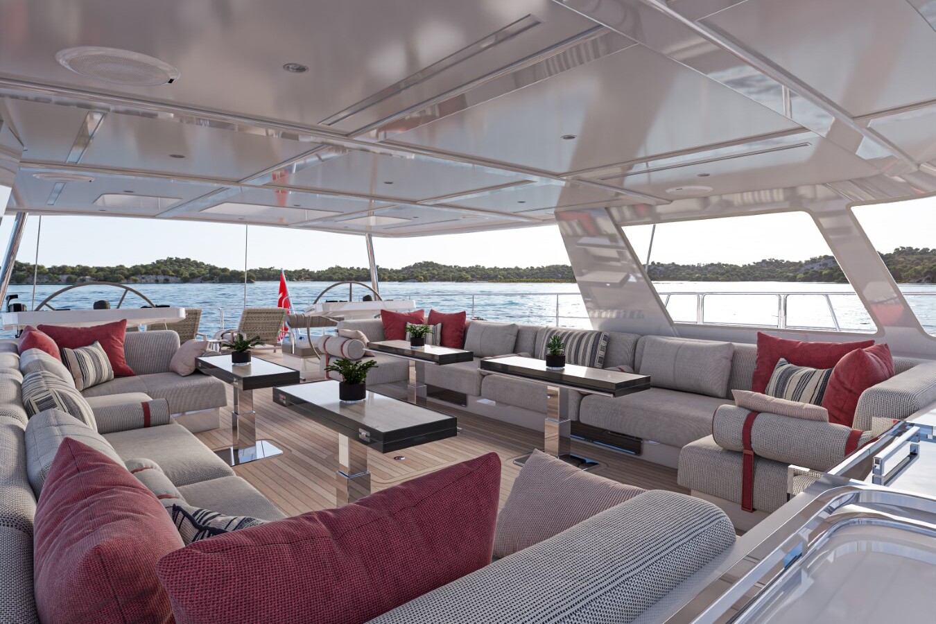 Meta Design Studio, Yacht Animation, 3D Animation, Yacht Rendering, 3D Rendering, Luxury Visualization, Yacht Visualization Luxurious yacht deck with gray sofas, red and striped pillows, coffee tables, and potted plants. Surrounded by water and distant greenery, under a sleek, shaded canopy. Relaxed and elegant outdoor seating arrangement.